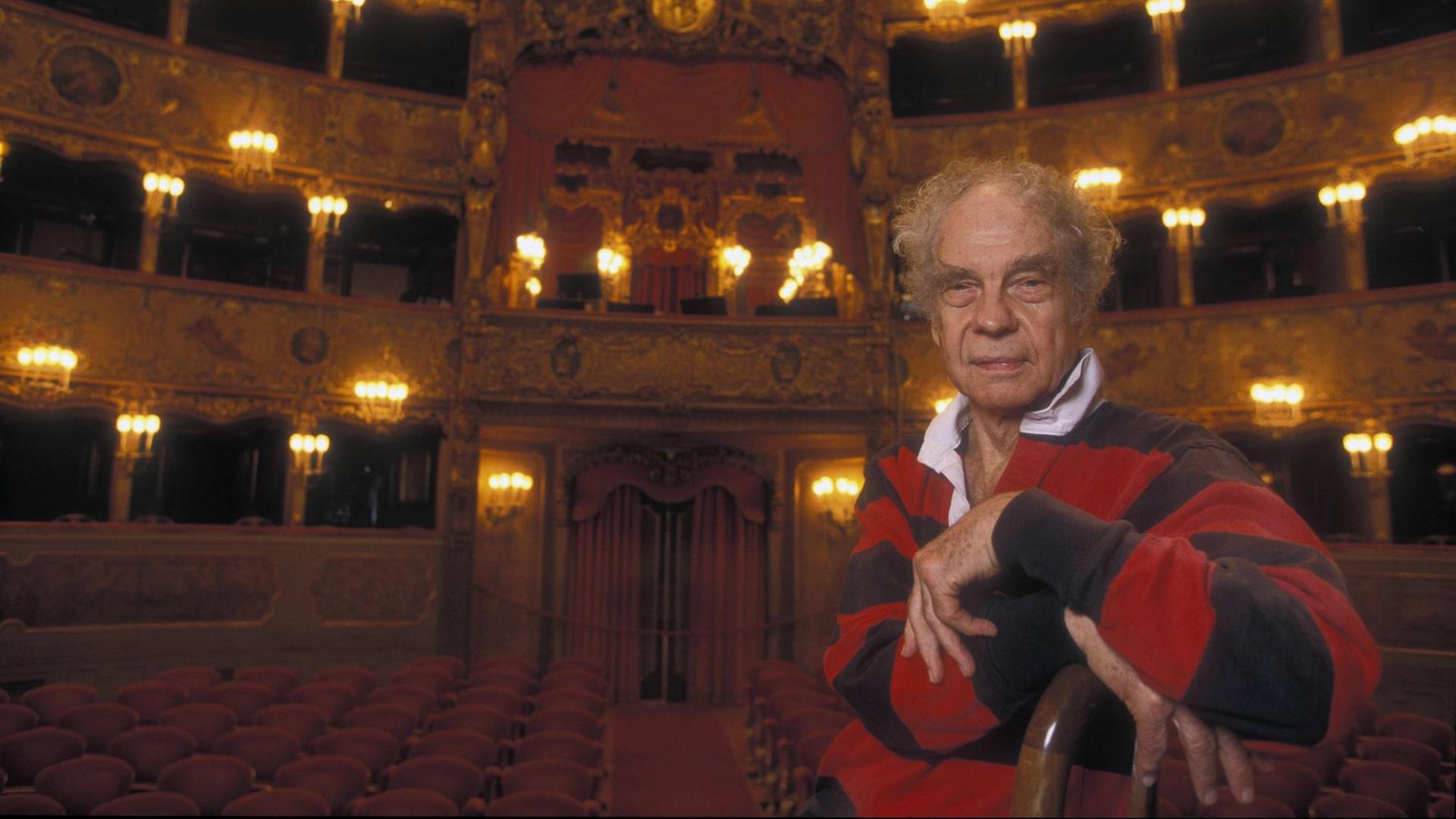 Der Choreograf Merce Cunningham sitzt im La Fenice Theater in Venedig auf einem Stuhl, im Hintergrund ist der Theatersaal mit rot bezogenen Stühlen und goldfarbenem Stuck zu sehen. Der Choreograf Merce Cunningham sitzt im La Fenice Theater in Venedig auf einem Stuhl, im Hintergrund ist der Theatersaal mit rot bezogenen Stühlen und goldfarbenem Stuck zu sehen.
