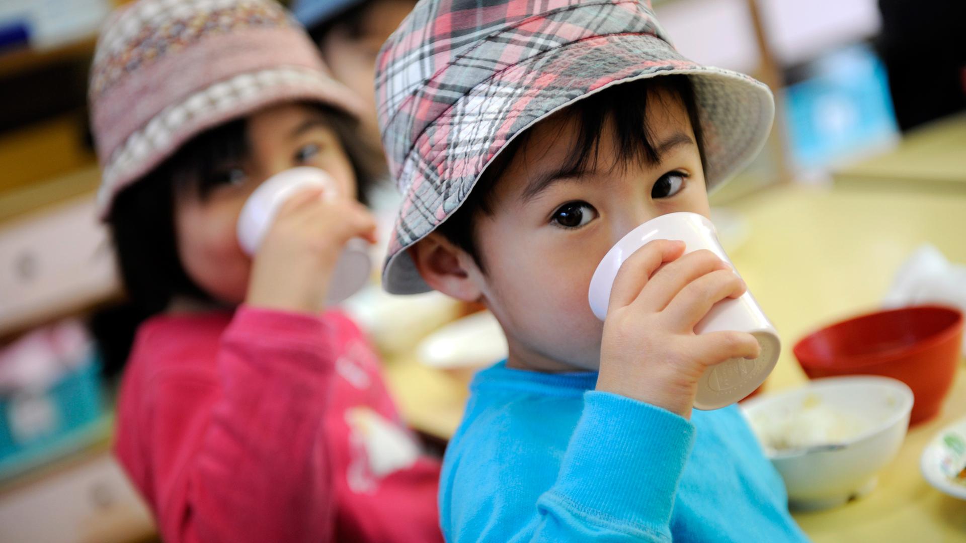 Japanische Kinder mit Hut, die aus Bechern trinken Japanische Kinder mit Hut, die aus Bechern trinken
