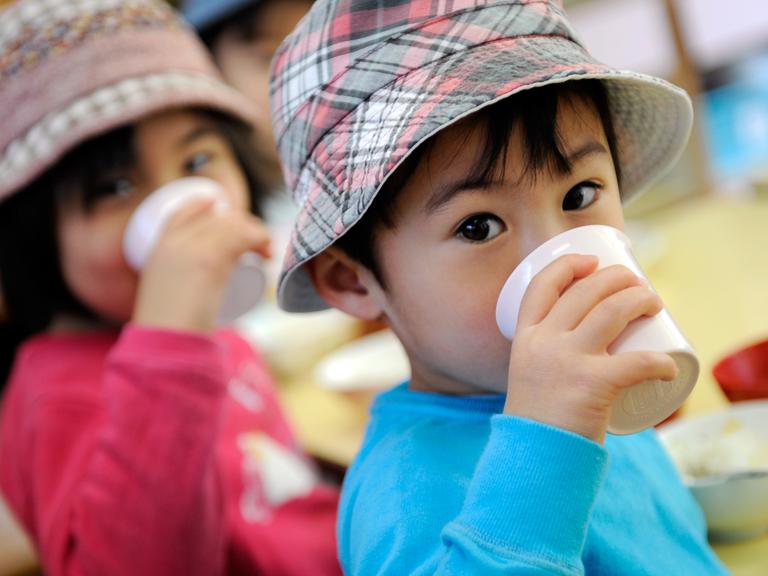 Japanische Kinder mit Hut, die aus Bechern trinken
