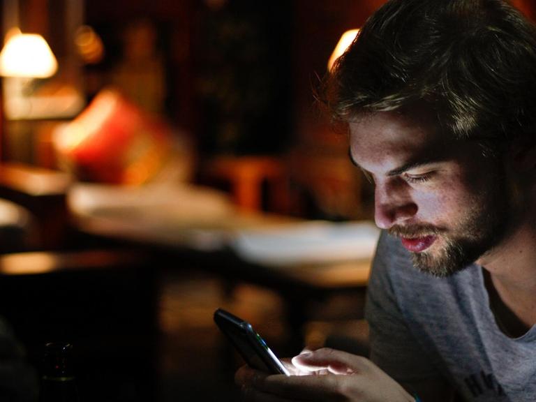 Während ein junger Mann auf sein Smartphone schaut, beleuchtet das Display sein Gesicht.