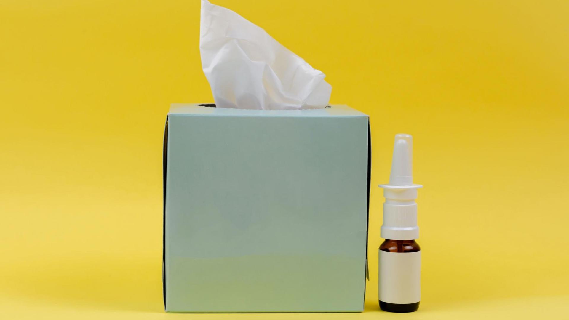 Eine Taschentuchbox und ein Fläschen Nasenspray vor gelbem Hintergrund Eine Taschentuchbox und ein Fläschen Nasenspray vor gelbem Hintergrund