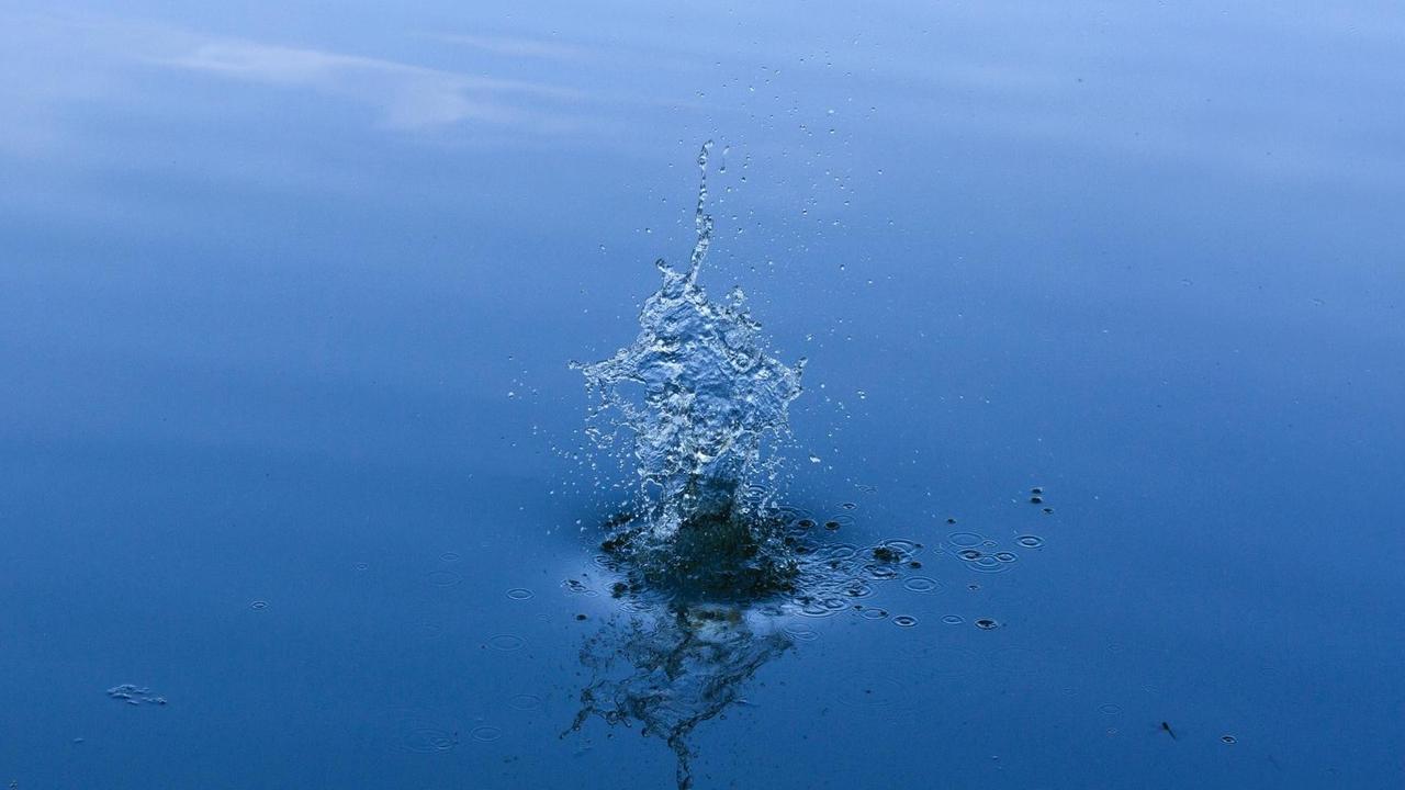 Ein Wasserspritzer in einer ruhigen blauen Wasseroberfläche. Ein Wasserspritzer in einer ruhigen blauen Wasseroberfläche.
