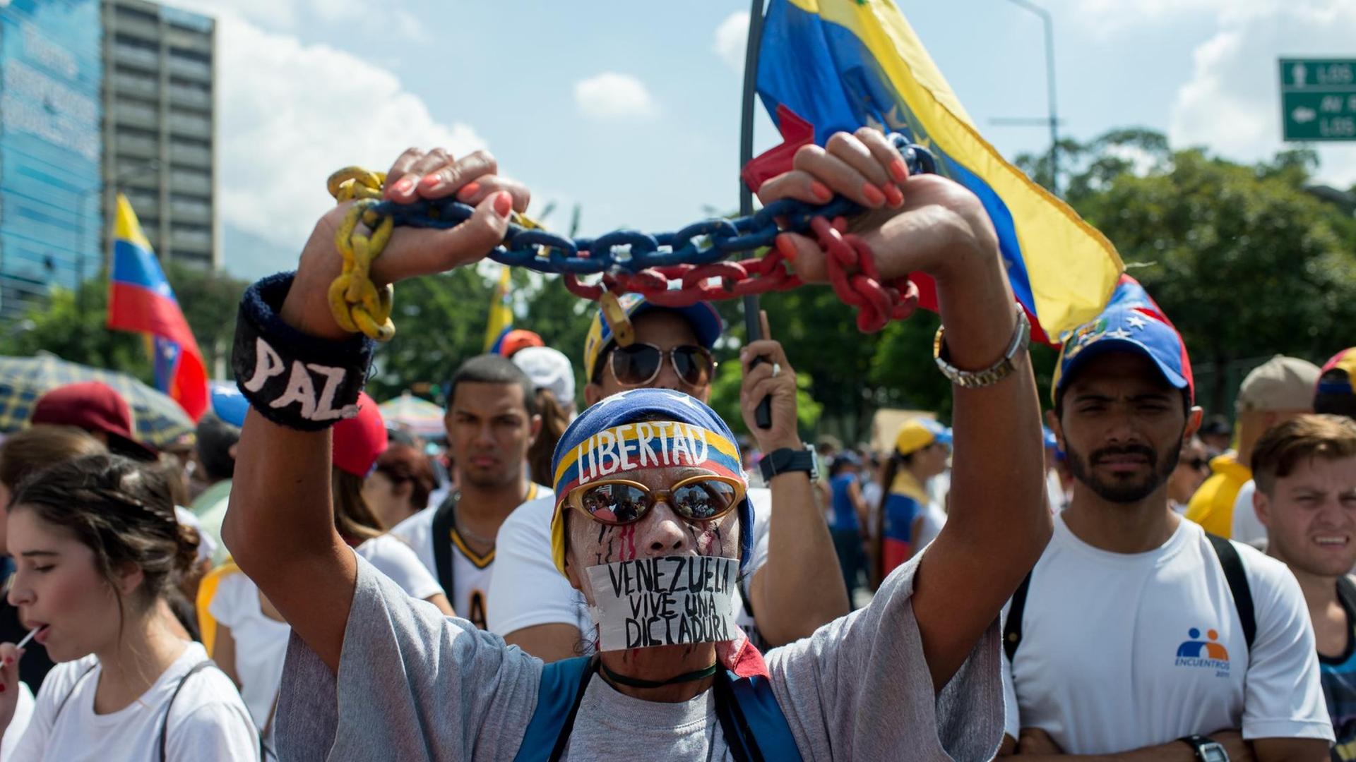 Ein Gegner von Präsident Maduro steht vor weiteren Demonstranten. Er hält eine Kette in seinen Händen; Zudem trägt er ein Stirnband mit der Aufschrift "Libertad". Ein Gegner von Präsident Maduro steht vor weiteren Demonstranten. Er hält eine Kette in seinen Händen; Zudem trägt er ein Stirnband mit der Aufschrift "Libertad".