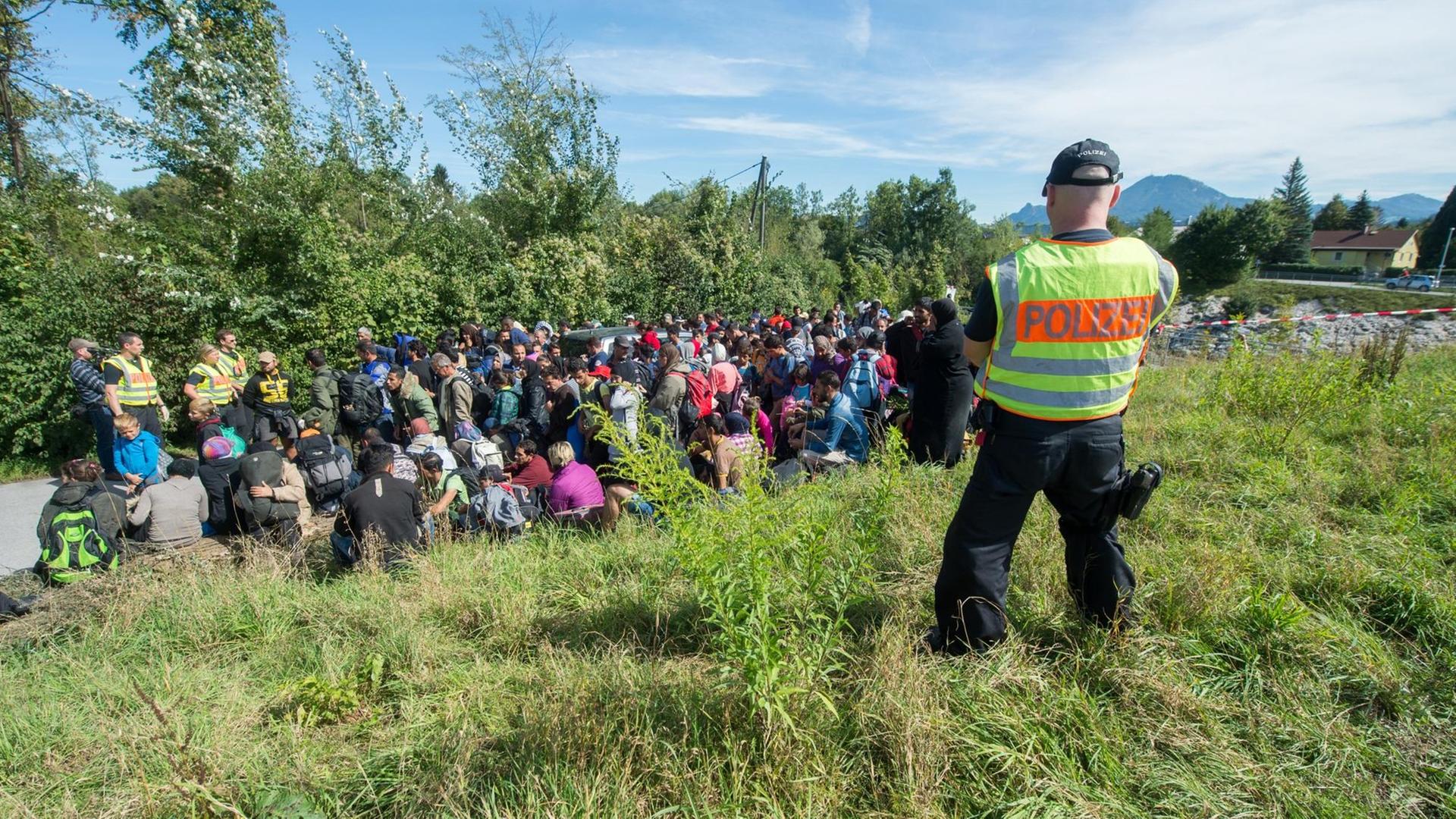 Flüchtlinge stehen am 16.09.2015 an der Salzach nahe der deutsch-österreichischen Grenze zwischen Salzburg und Freilassing (Bayern) hinter einem Bundespolizisten. Flüchtlinge stehen am 16.09.2015 an der Salzach nahe der deutsch-österreichischen Grenze zwischen Salzburg und Freilassing (Bayern) hinter einem Bundespolizisten.