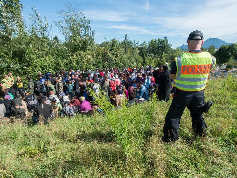 Flüchtlinge stehen am 16.09.2015 an der Salzach nahe der deutsch-österreichischen Grenze zwischen Salzburg und Freilassing (Bayern) hinter einem Bundespolizisten.