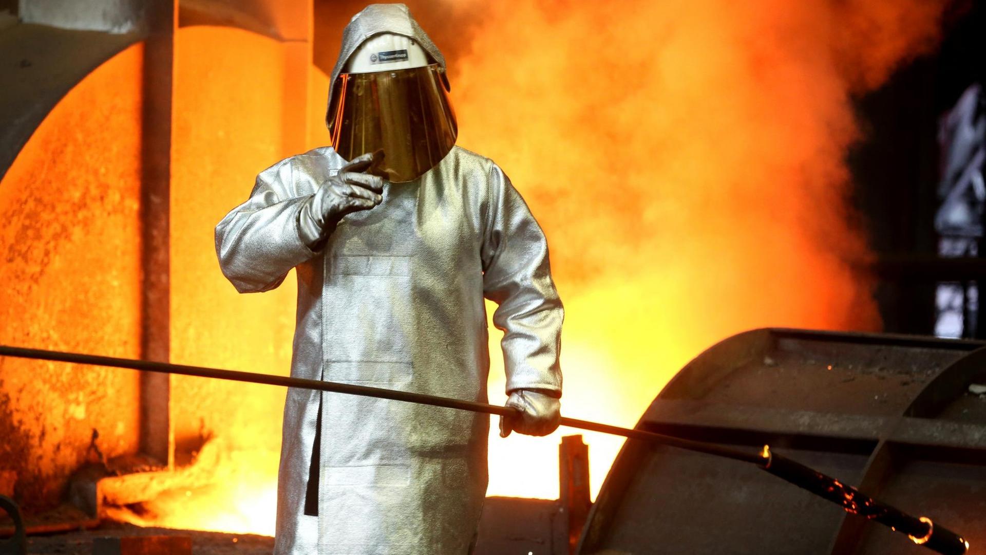 Ein Stahlarbeiter prüft am Hochofen 8 bei ThyssenKrupp in Duisburg (Nordrhein-Westfalen) die Stahlqualität nach dem Abstich. Im Hintergrund sind Glut und Flammen zu sehen. Ein Stahlarbeiter prüft am Hochofen 8 bei ThyssenKrupp in Duisburg (Nordrhein-Westfalen) die Stahlqualität nach dem Abstich. Im Hintergrund sind Glut und Flammen zu sehen.