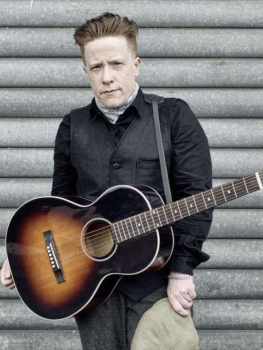 Remco steht mit einer umgehängten Gitarre vor einer Wand.