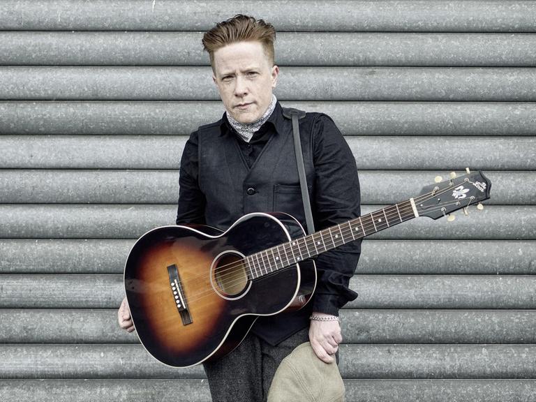 Remco steht mit einer umgehängten Gitarre vor einer Wand.