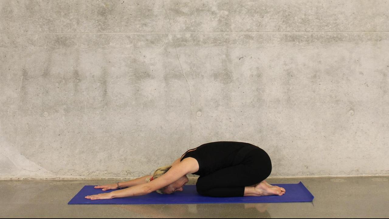 Eine sportliche Frau macht eine Yoga-Übung auf einer blauen Matte vor einer Sichtbeton-Wand. Eine sportliche Frau macht eine Yoga-Übung auf einer blauen Matte vor einer Sichtbeton-Wand.