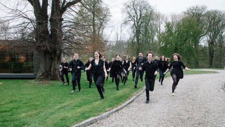 Die Musiker des Stegreiforchesters laufen über eine Wiese in einem Park. Die Musiker des Stegreiforchesters laufen über eine Wiese in einem Park.