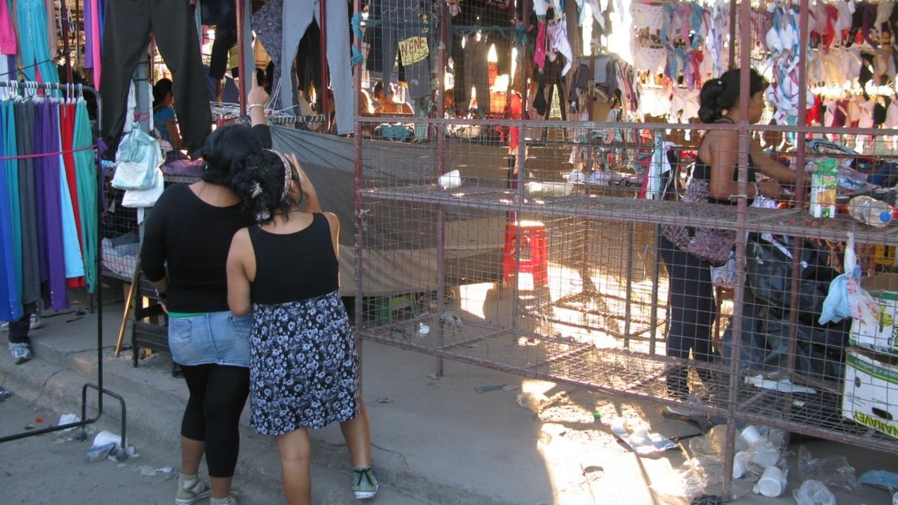 Zwei junge Frauen stehen auf dem Markt La Salada in Buenos Aires und betrachten Textilien, die verkauft werden.