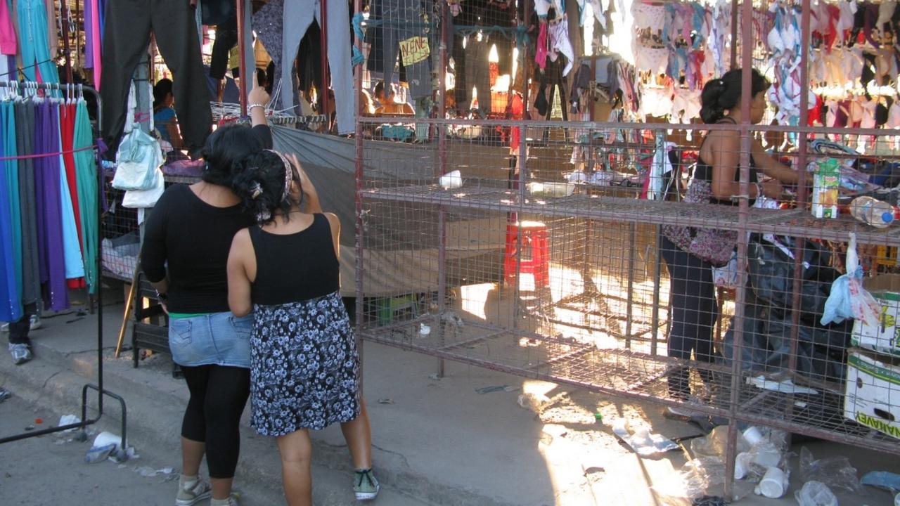 Zwei junge Frauen stehen auf dem Markt La Salada in Buenos Aires und betrachten Textilien, die verkauft werden. Zwei junge Frauen stehen auf dem Markt La Salada in Buenos Aires und betrachten Textilien, die verkauft werden.