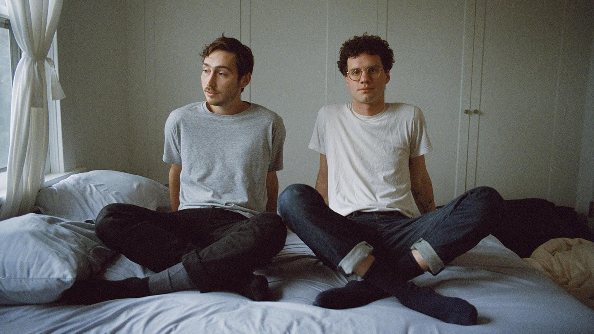 Julien Ehrlich und Max Kakacek sitzen auf einem Bett Julien Ehrlich und Max Kakacek sitzen auf einem Bett