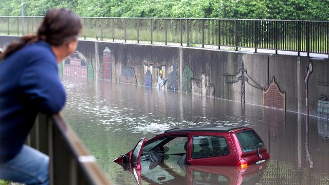 Ein Mann schaut sich am 30.05.2016 in Oberhausen (Nordrhein-Westfalen) ein Auto in einer überfluteten Straßenunterführung an.