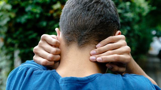 Ein autistischer junger Mann, fotografiert von hinten, er hält sich die Ohren zu.