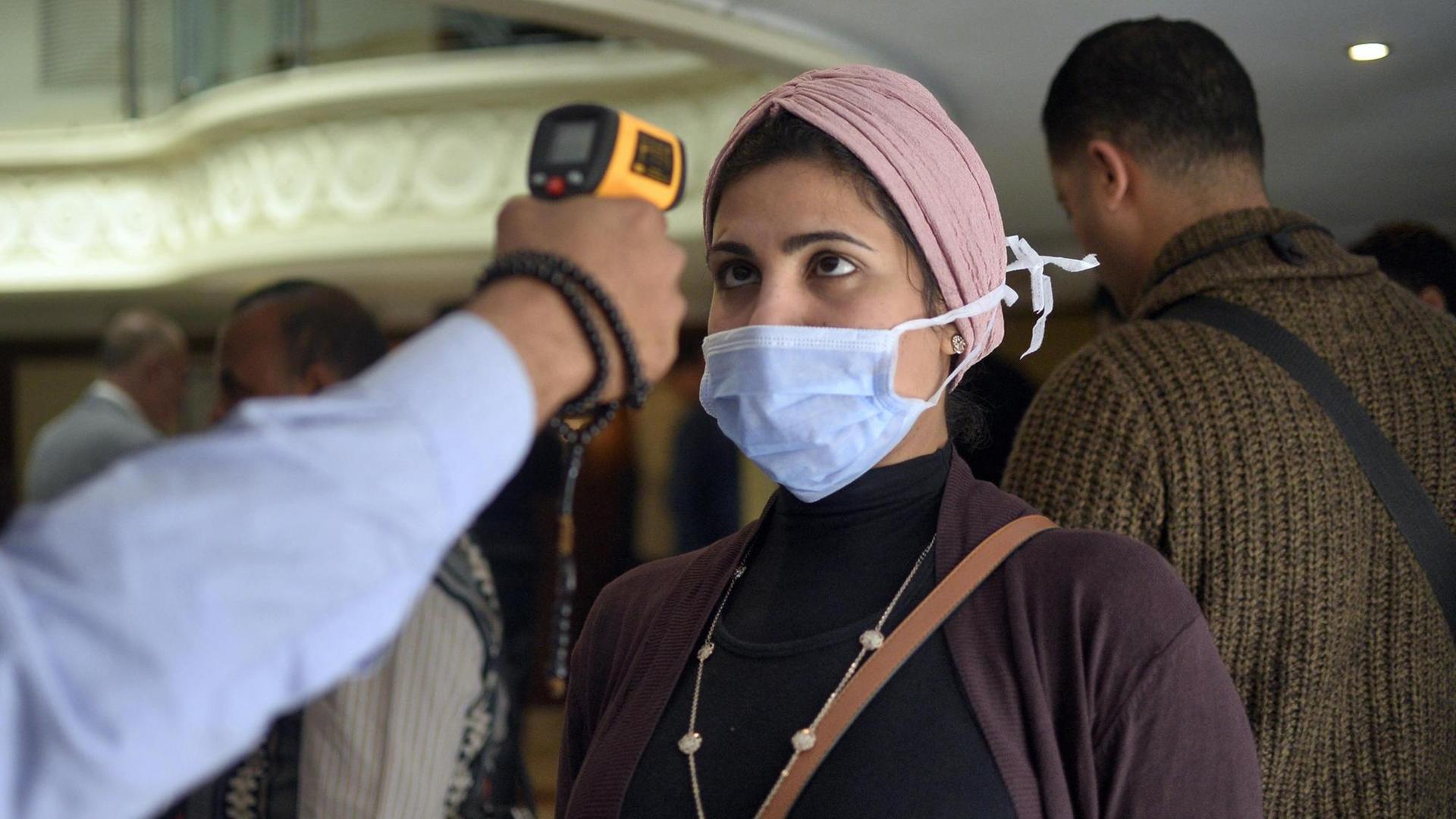 Einer Frau mit Maske wird auf einem Boot in der ägyptischen Stadt Luxor die Körpertemperatur gemessen. Einer Frau mit Maske wird auf einem Boot in der ägyptischen Stadt Luxor die Körpertemperatur gemessen.