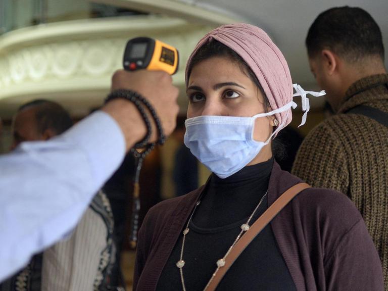 Einer Frau mit Maske wird auf einem Boot in der ägyptischen Stadt Luxor die Körpertemperatur gemessen.