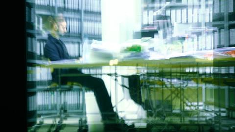 Ein Mann sitzt abends in einem Büro an einem vollen Schreibtisch und arbeitet in Berlin.