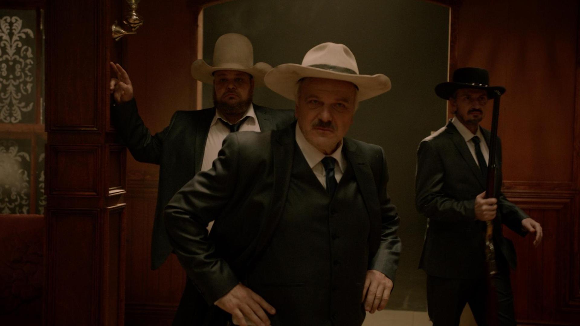 Drei Männer mit Cowboyhüten betreten einen Westernsalon.