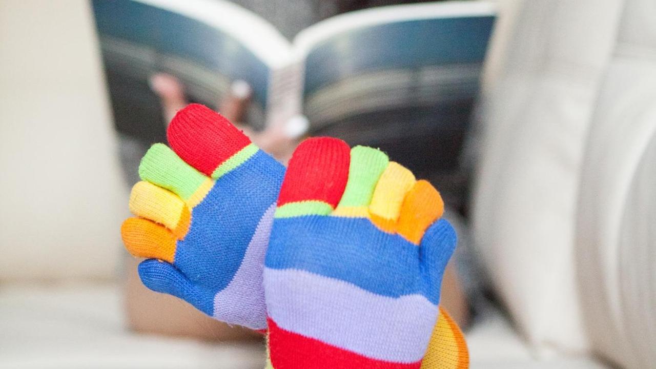Eine Frau mit regenbogenfarbenen Socken liest auf dem Sofa. Eine Frau mit regenbogenfarbenen Socken liest auf dem Sofa.