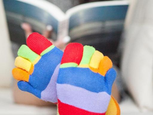 Eine Frau mit regenbogenfarbenen Socken liest auf dem Sofa.