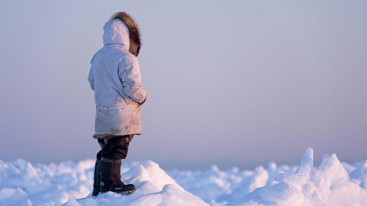 Ein Mann der Inupiaq steht auf dem Eis und schaut aufs Eis.