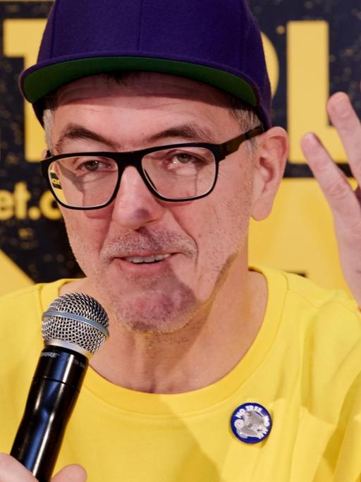 Loveparade-Gründer Dr. Motte stellt bei einer Pressekonferenz in Berlin sein neues Projekt "Rave the Planet" vor. Er trägt einen gelben Pullover und eine dunkelblaue Mütze.