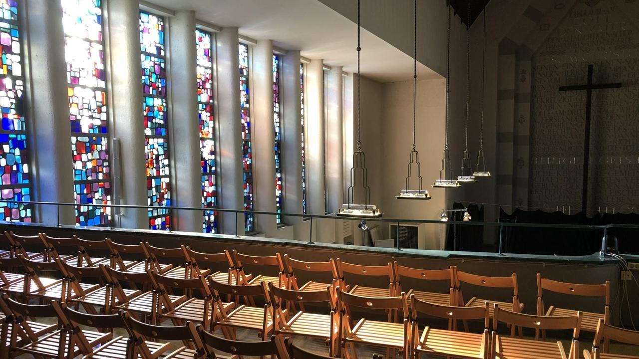 Leere Klappstühle stehen vor den Kirchenfenstern mit Blick in den modernen Kirchenraum hinein. Leere Klappstühle stehen vor den Kirchenfenstern mit Blick in den modernen Kirchenraum hinein.
