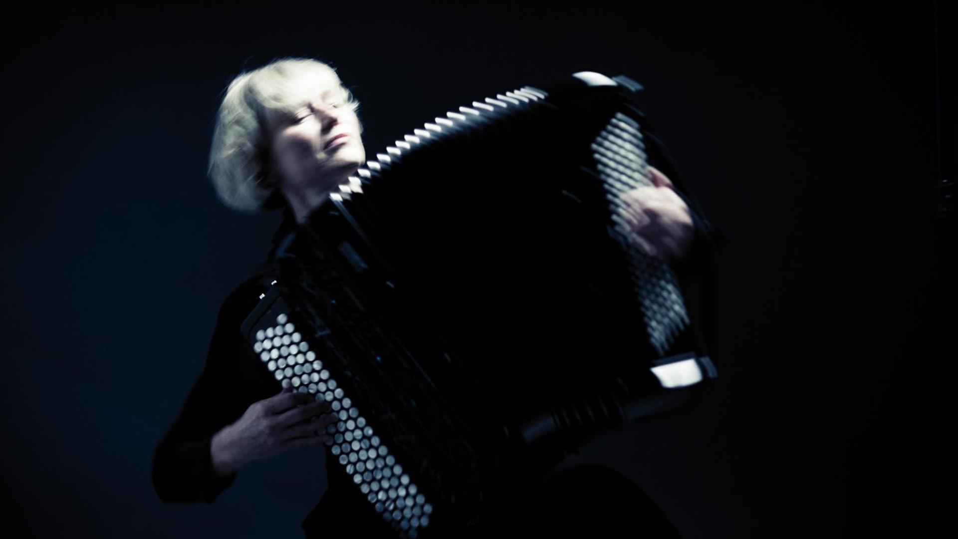 Musikerin spielt Knopfakkordeon in einem schwarzen Raum Musikerin spielt Knopfakkordeon in einem schwarzen Raum