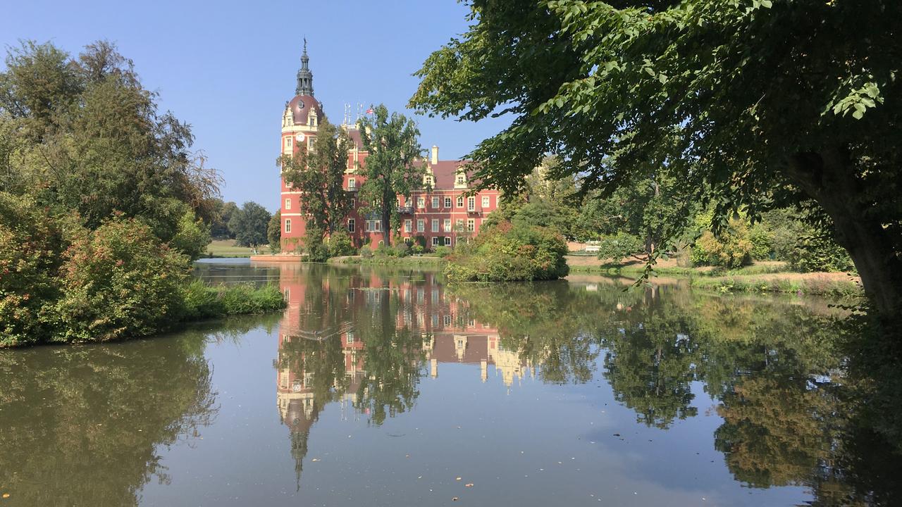 Das rosafarbene Schloss Bad Muskau spiegelt sich in einem See. Das rosafarbene Schloss Bad Muskau spiegelt sich in einem See.