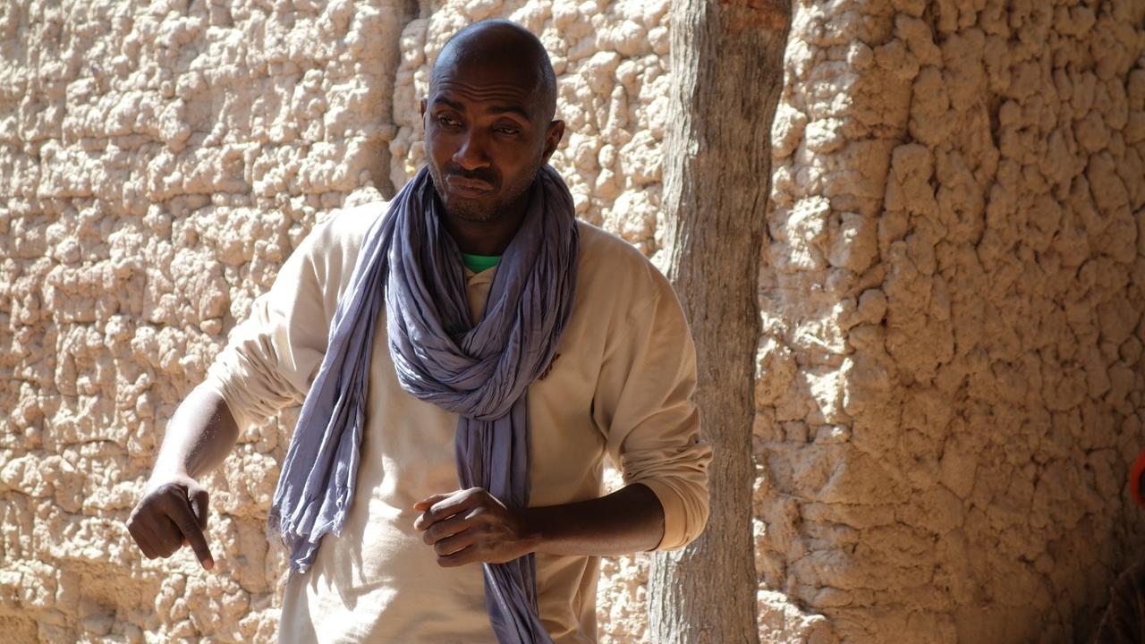 Vermittler Oumar Maiga steht vor einem Haus und spricht. Vermittler Oumar Maiga steht vor einem Haus und spricht.