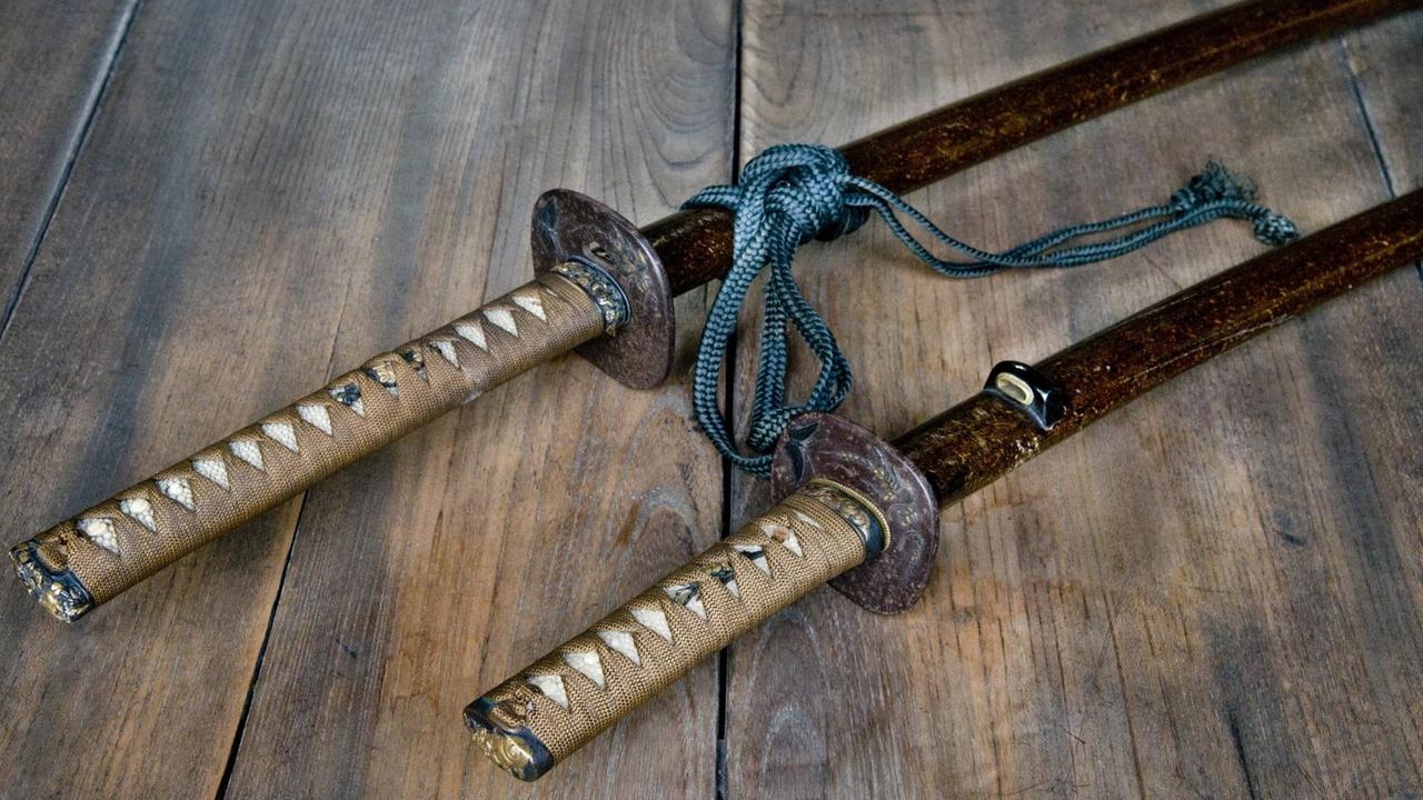 Zwei traditionelle japanische Schwerter liegen auf einer Holzfläche Zwei traditionelle japanische Schwerter liegen auf einer Holzfläche