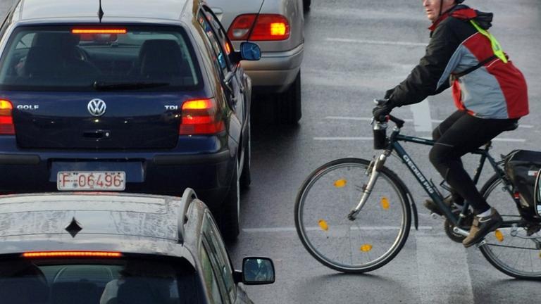 Ein Fahrradfahrer fährt zwischen Autos vorbei, die sich an einer Einfallstraße von Frankfurt am Main im Berufsverkehr stauen. Ein Fahrradfahrer fährt zwischen Autos vorbei, die sich an einer Einfallstraße von Frankfurt am Main im Berufsverkehr stauen.