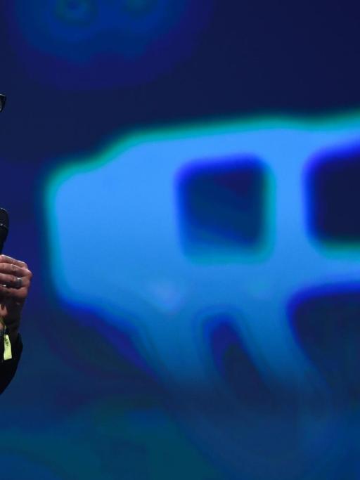 Der kanadische Science-Fiction-Autor Cory Doctorow auf einer Bühne. Im Hintergrund ein auf eine Wand projiziertes überdimensioniertes Megafon.