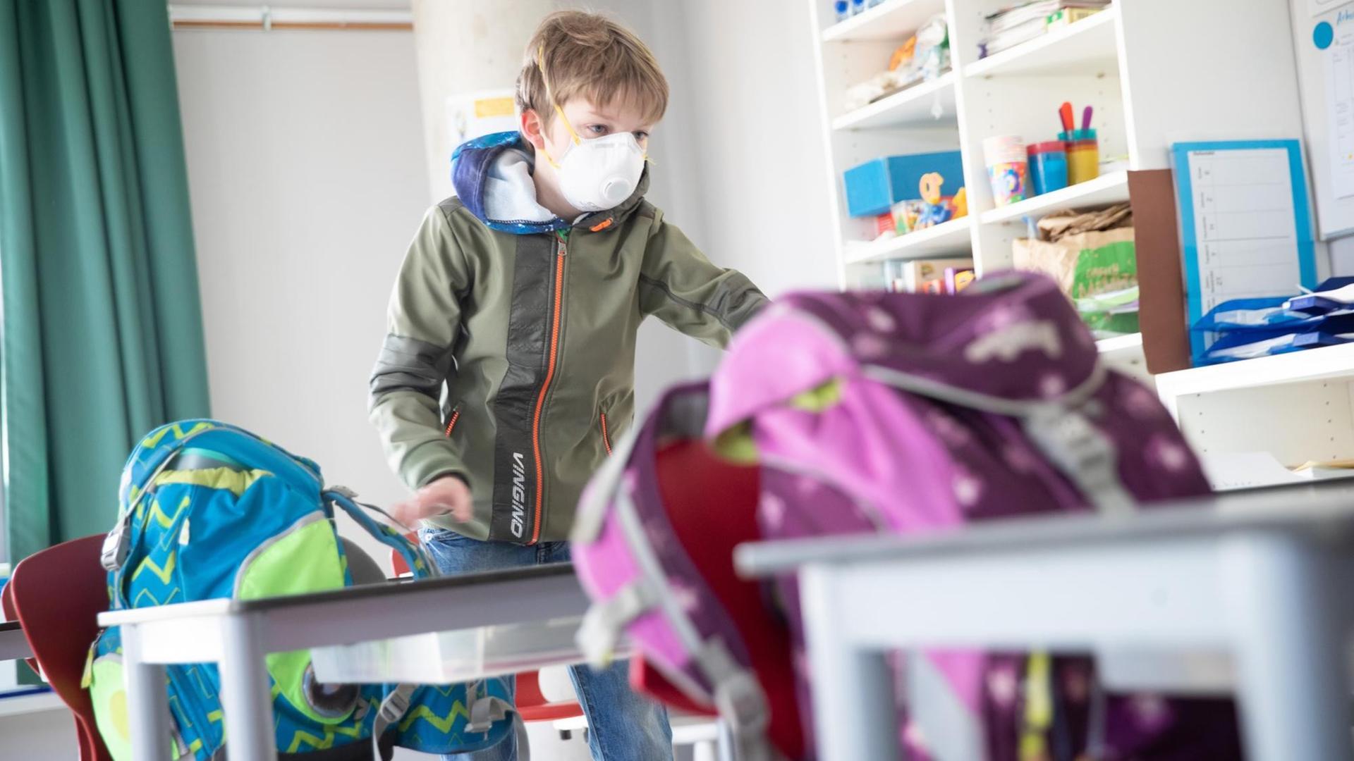 Ein Grundschüler mit Mundschutz stellt seine Ranzen im Klassenzimmer ab. Ein Grundschüler mit Mundschutz stellt seine Ranzen im Klassenzimmer ab.