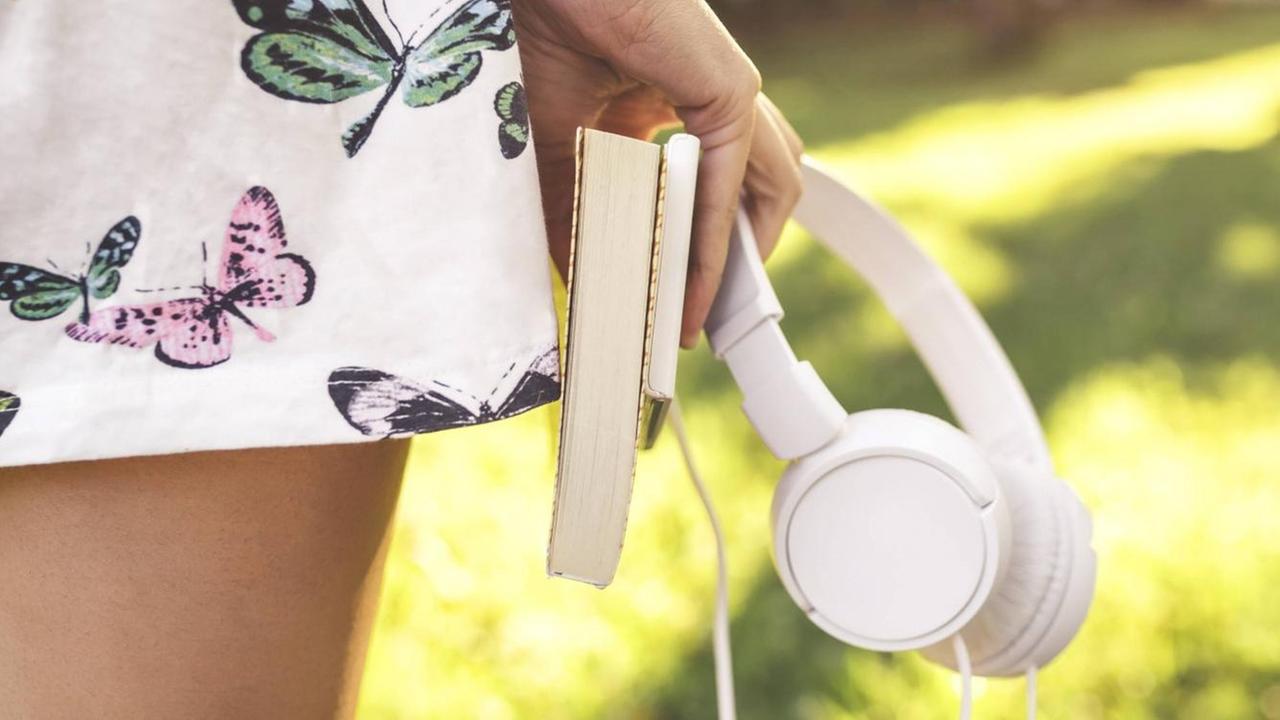 In Köln wird der Deutsche Hörbuchpreis verliehen - eine junge Frau hält einen Kopfhörer und ein Buch in der Hand (Symbolbild) In Köln wird der Deutsche Hörbuchpreis verliehen - eine junge Frau hält einen Kopfhörer und ein Buch in der Hand (Symbolbild)