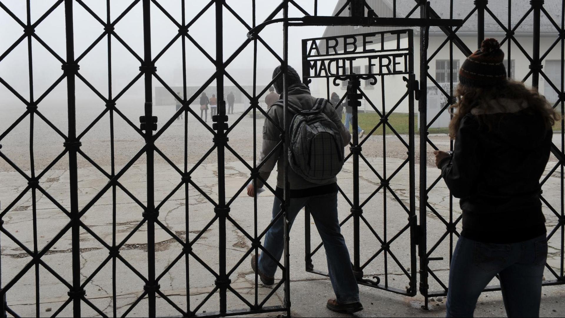 "Arbeit macht frei" steht am 19.11.2012 an einem Tor zum ehemaligen Konzentrationslager in Dachau nahe München. Zwei Menschen gehen nacheinander hindurch.