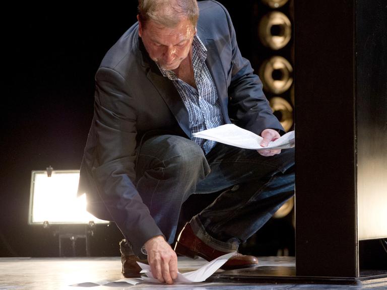 Rene Pollesch sammelt während der Verleihung des Theaterpreises die heruntergefallenen Blätter seines Redemanuskripts vom Boden auf.