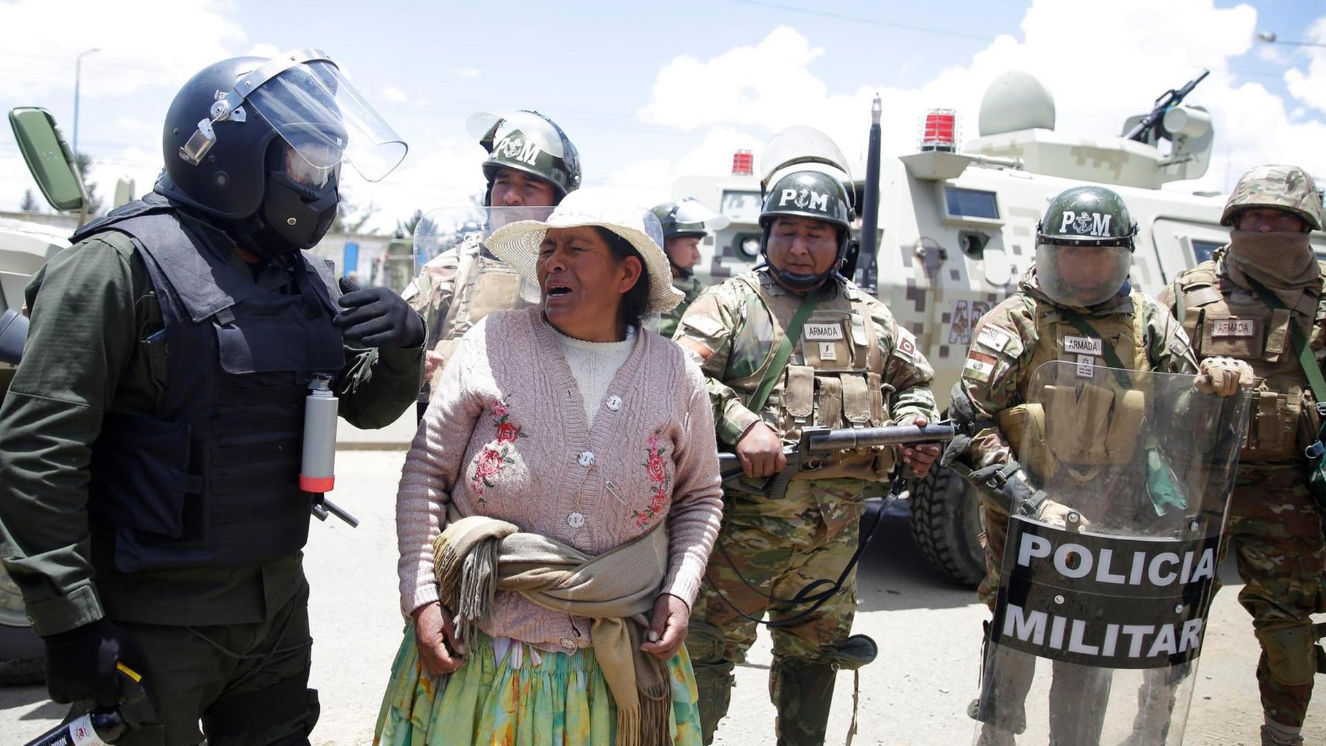 Protest am Eingang der Treibstoffanlage Senkata in der Stadt El Alto. Eine Frau mit verzerrten Gesicht ist zwischen mehreren Soldaten zu sehen. Protest am Eingang der Treibstoffanlage Senkata in der Stadt El Alto. Eine Frau mit verzerrten Gesicht ist zwischen mehreren Soldaten zu sehen.