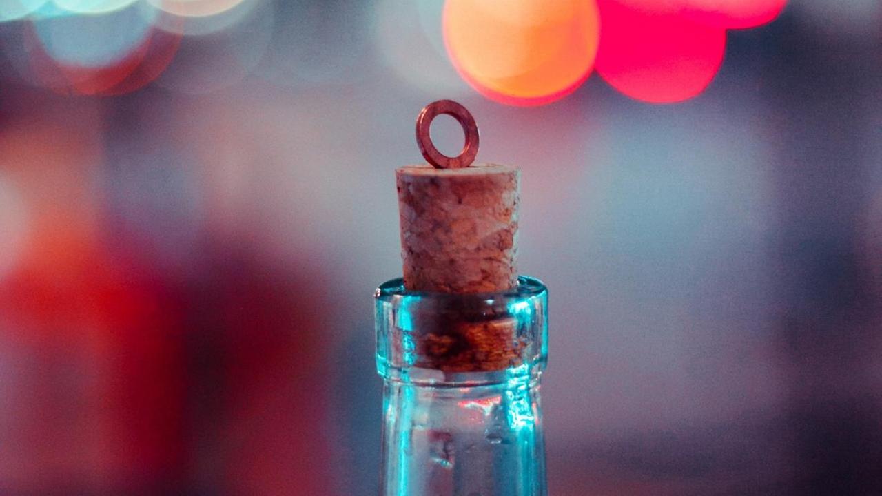 Ein Korken steckt in einer Flasche, im Hintergrund des Bildes sind unscharfe rote und blaue Lichter zu sehen. Ein Korken steckt in einer Flasche, im Hintergrund des Bildes sind unscharfe rote und blaue Lichter zu sehen.