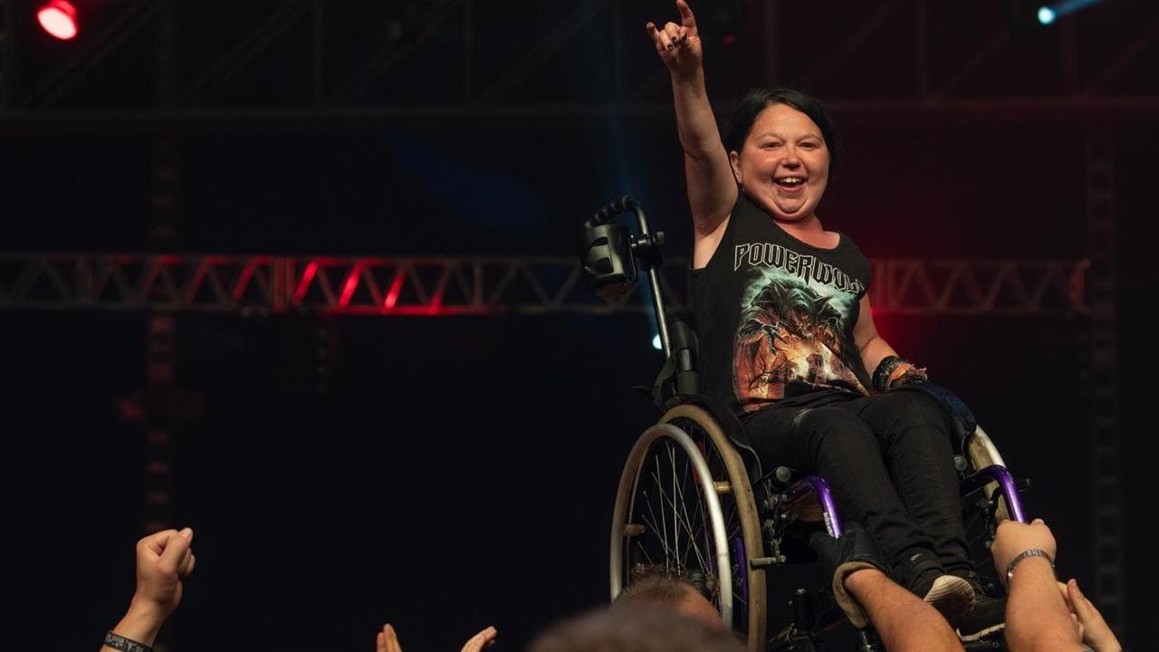 Wacken Open Air 2018, Frau im Rollstuhl steht am Bühnenrand vor begeistertem Publikum, im Hintergrund eine dunkle Bühne Wacken Open Air 2018, Frau im Rollstuhl steht am Bühnenrand vor begeistertem Publikum, im Hintergrund eine dunkle Bühne