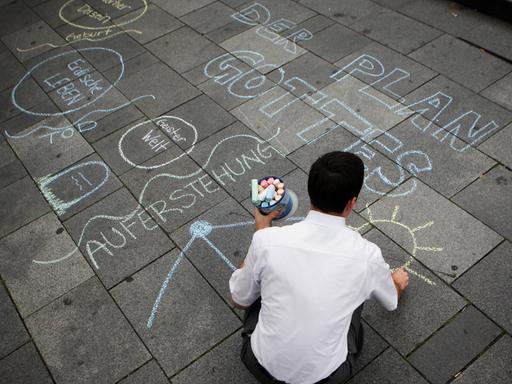 Ein Missionar der Mormonen malt unter anderem "Der Plan Gottes" auf den Boden einer Fußgängerzone.