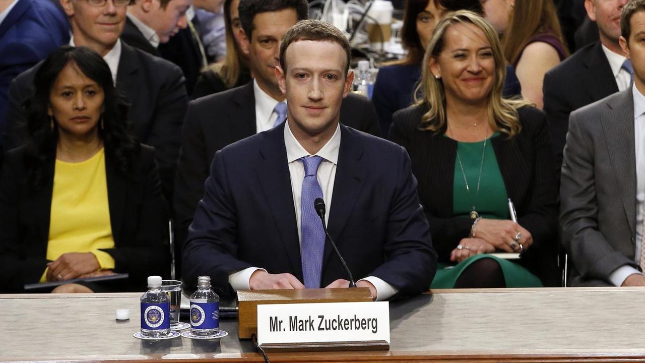 Mark Zuckerberg sitzt an einem Tisch in einem Raum des US-Kongresses, hinter ihm eine Gruppe von Menschen Mark Zuckerberg sitzt an einem Tisch in einem Raum des US-Kongresses, hinter ihm eine Gruppe von Menschen
