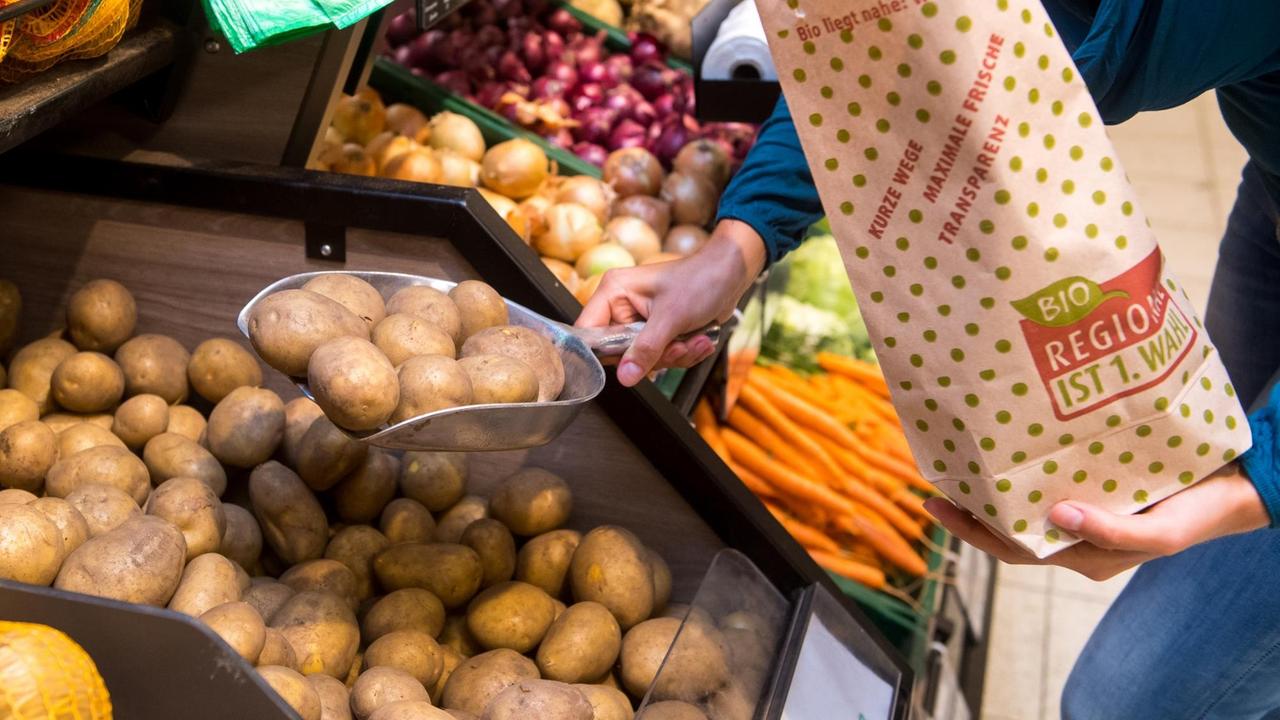 Jemand füllt in einem Supermarkt lose Kartoffeln in eine Papiertüte Jemand füllt in einem Supermarkt lose Kartoffeln in eine Papiertüte