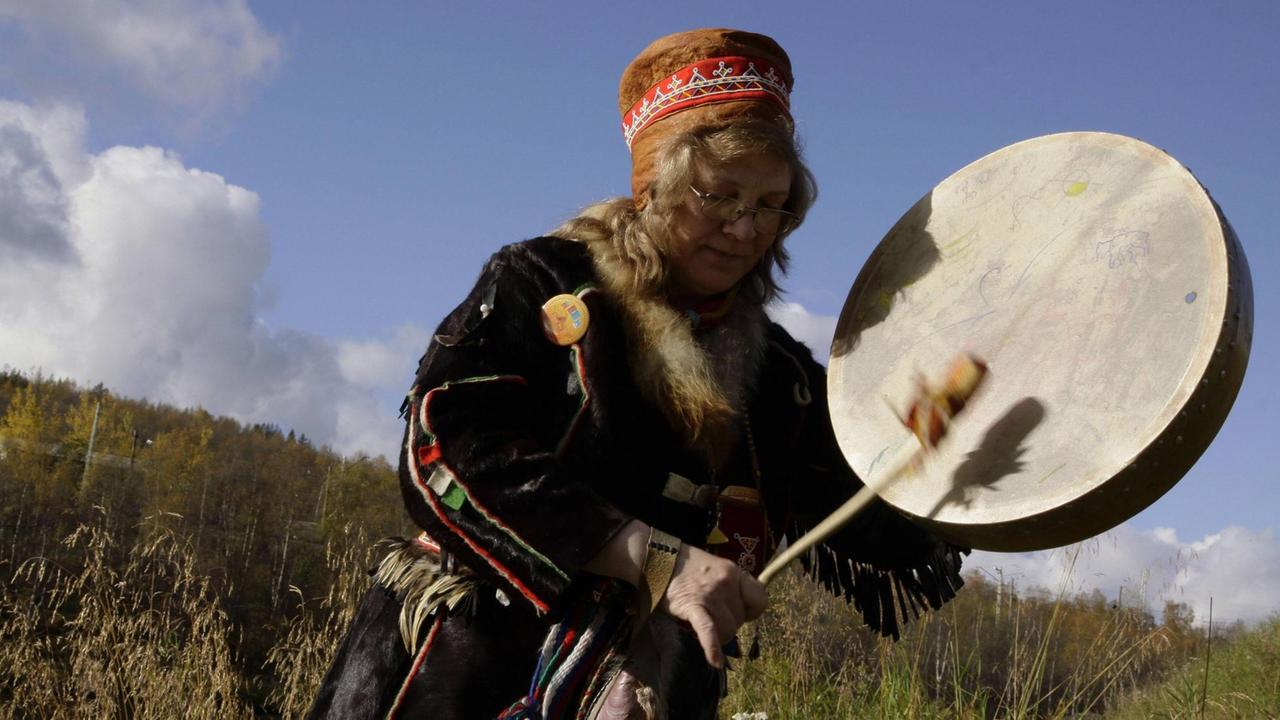 Schamanin in traditioneller samischer Kleidung beim Trommeln.