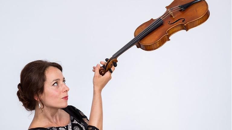 Die Geigerin hält ihr Instrument gewagt schräg in die Höhe. Die Geigerin hält ihr Instrument gewagt schräg in die Höhe.