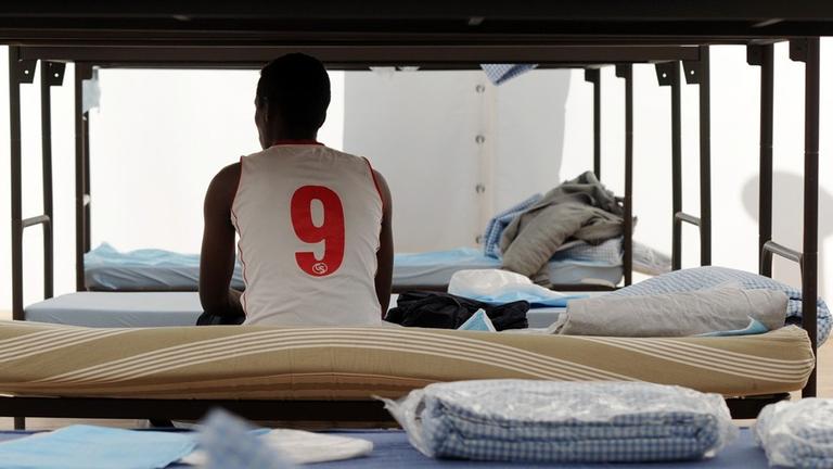 Ein Flüchtling sitzt in München in einem Unterkunftszelt am Internationalen Jugendübernachtungscamp am Kapuzinerhölzl in seinem Bett. Ein Flüchtling sitzt in München in einem Unterkunftszelt am Internationalen Jugendübernachtungscamp am Kapuzinerhölzl in seinem Bett.