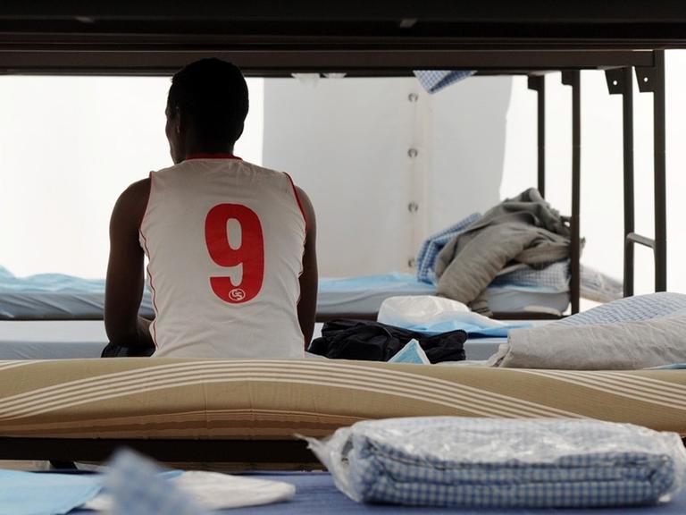 Ein Flüchtling sitzt in München in einem Unterkunftszelt am Internationalen Jugendübernachtungscamp am Kapuzinerhölzl in seinem Bett.