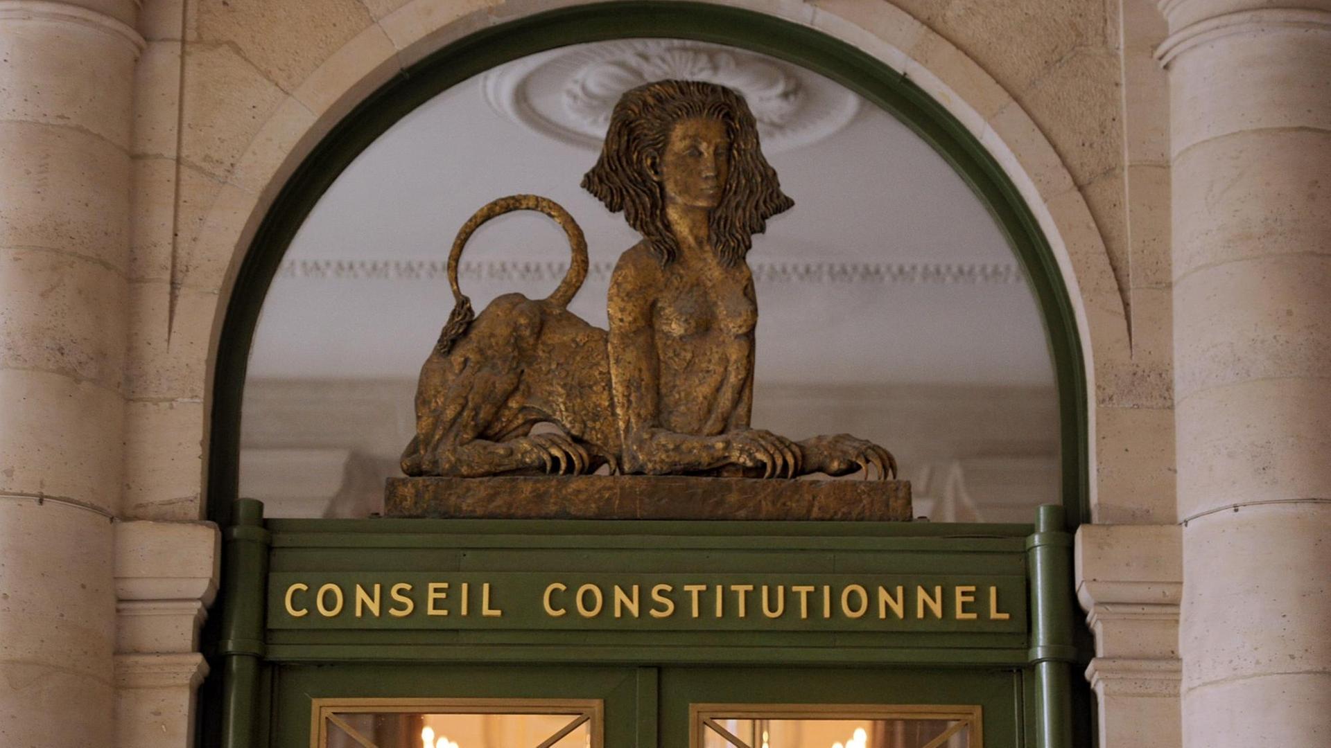 Der Eingang des Verfassungsgerichts in Paris. Eine Statue, halb Frau, halb Löwe, liegt auf einem Stein, darunter der Schriftzug Conseil Constitutionnel.