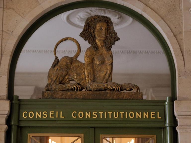 Der Eingang des Verfassungsgerichts in Paris. Eine Statue, halb Frau, halb Löwe, liegt auf einem Stein, darunter der Schriftzug Conseil Constitutionnel.